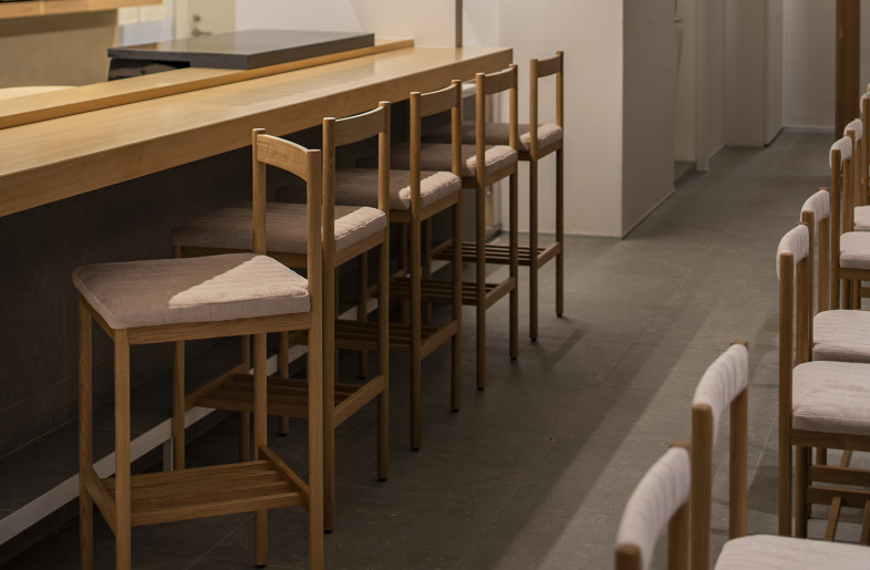 Custom oak counter chairs with bag shelves below have backrests in line with the counter to create a neat spatial impression. - Keishiro Yamada