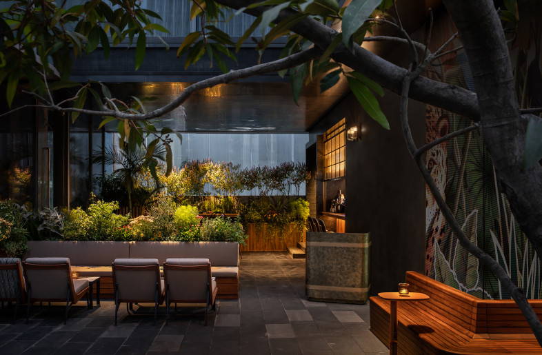 Extending from the side of the building is a metal eave, leading the way to an "inner courtyard" enveloped by verdant greenery. This area, reminiscent of a tranquil street garden, is perfumed by the nearby cooking and a subtle note of wine, extending a welcoming invitation to all. - Ting Wang