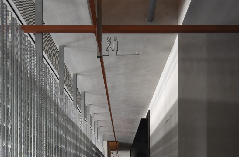 The aisle: Perforated galvanized steel wave plates demarcate the public corridor from the open office area, filling the pathway with the sheen as well as the leaping seasonal lights and shadows reflected on the bare concrete walls. - Rongkun Chen