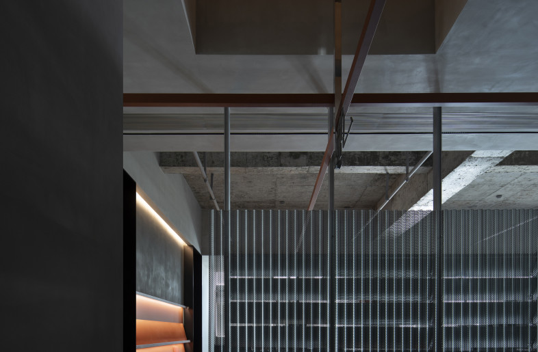 The aisle: Perforated galvanized steel wave plates demarcate the public corridor from the open office area, filling the pathway with the sheen as well as the leaping seasonal lights and shadows reflected on the bare concrete walls. - Rongkun Chen