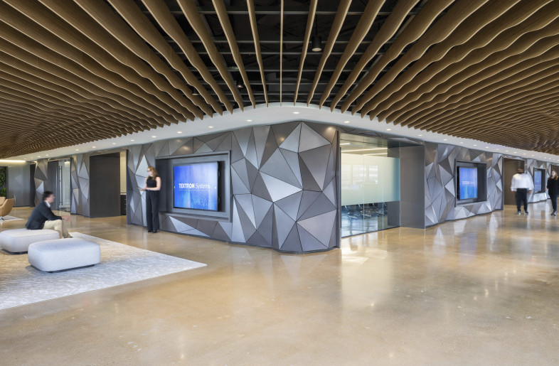 A gallery corridor serves as a dynamic spine through the space. It features interactive displays set within faceted wall panels and anchored by a sculptural ceiling that adds movement and cohesion. - Evan Thomas/studiothomas