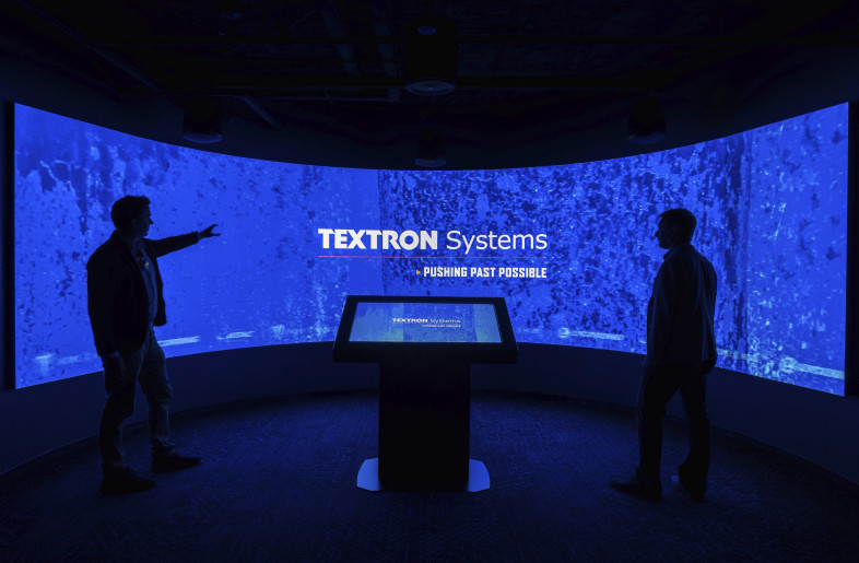 An immersive theater environment with a curved digital wall and central touchscreen invites visitors to engage with Textron Systems’ story through a high-impact and interactive brand experience. - Evan Thomas/studiothomas