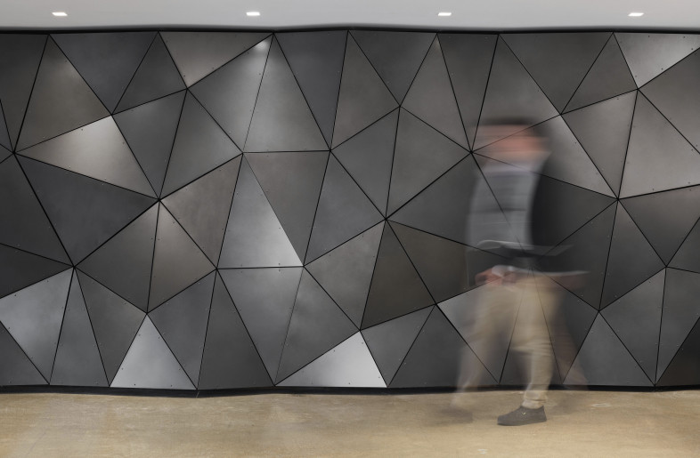 A bold feature wall composed of faceted metal panels delivers a sense of movement and materiality, serving as both an architectural focal point and a symbol of precision engineering. - Evan Thomas/studiothomas
