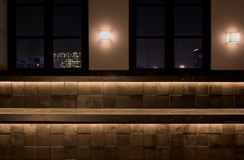 Detail of the café counter, featuring a grid of end-grain charred wood blocks illuminated by soft underlighting. - Ye Rin Mok