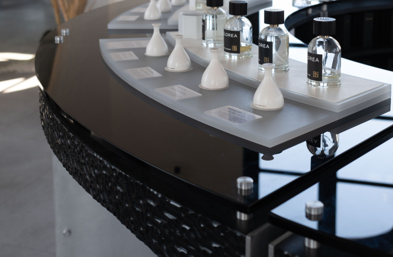 Detail view of Elorea’s curved fragrance display, showcasing the interplay of glossed black glass, sculpted wood, and perfume testers under soft daylight. - Ye Rin Mok