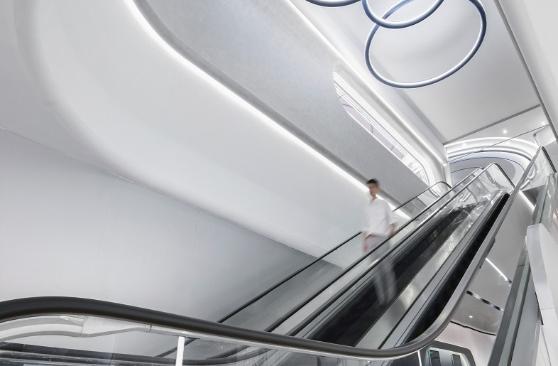 Taking the escalator down from the lobby, the soaring ceiling height and streamlined light trough design create a spaceship-like atmosphere, guiding audiences to another floor. - Design Action