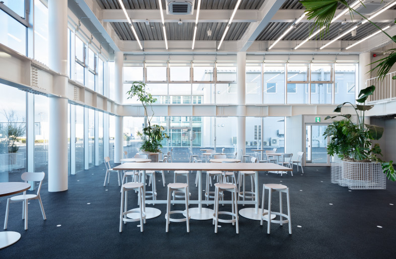 Cafeteria. The same movable plantings are placed as outside. The ground floor has no boundary with the site and the finishes and graphics of the floor are continuous. - Takumi Ota