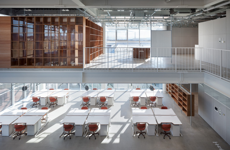 Looking down from the fourth floor through the atrium to an office area on the third floor. The grid also appears as raceways on the ceiling. Movable interfaces such as whiteboards and storage shelves are hooked up to one axis of the grid, while the other axis is fitted with lighting. - Takumi Ota