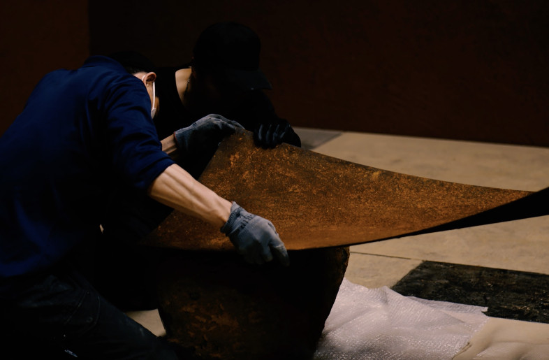 Rusted, curved steel plates, dug out of the red clay, are fixed to the Daté Kan Stone. It is, as it were, a reunion of material memories through rust. - Hiroshi Sato