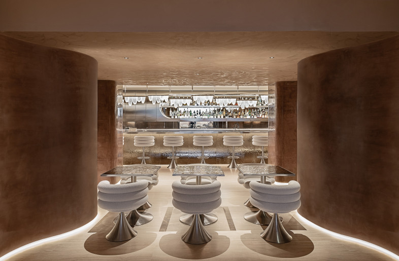 The bistro is conceived as a place of gathering, pause, and discovery of culinary excellence, immersed in a warm and sophisticated atmosphere. Here, the curved and sensual walls envelop guests, creating a sense of intimacy and conviviality. Mocha mousse hand spatulated color on the walls and  Voluptas stools and chairs designed by Studiopepe for Visionnaire - Max Zambelli
