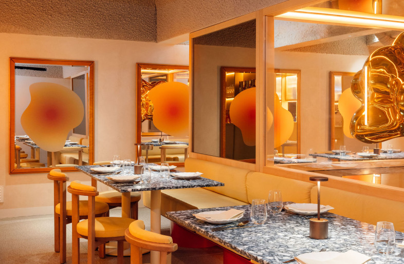 Downstairs, the space gets playful. Wavy glass blobs flirt with reflections, while marbled tabletops and chubby chairs line up like characters in a well-rehearsed script—each one doing its part in this warm, slightly surreal mise-en-scène. - Francisco Nogueira