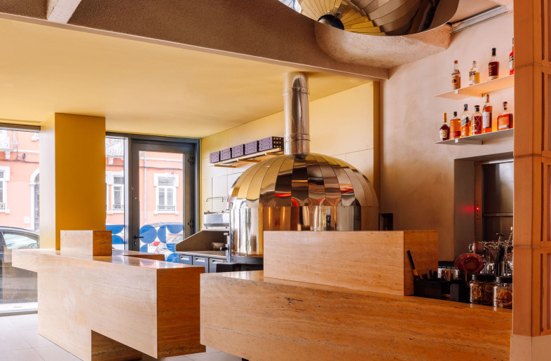 A choreography of travertine volumes defines the bar and reception, framing the heart of the kitchen—the custom stainless steel oven. Above, a mirrored ceiling amplifies the activity below, blending craft, heat, and reflection. - Francisco Nogueira