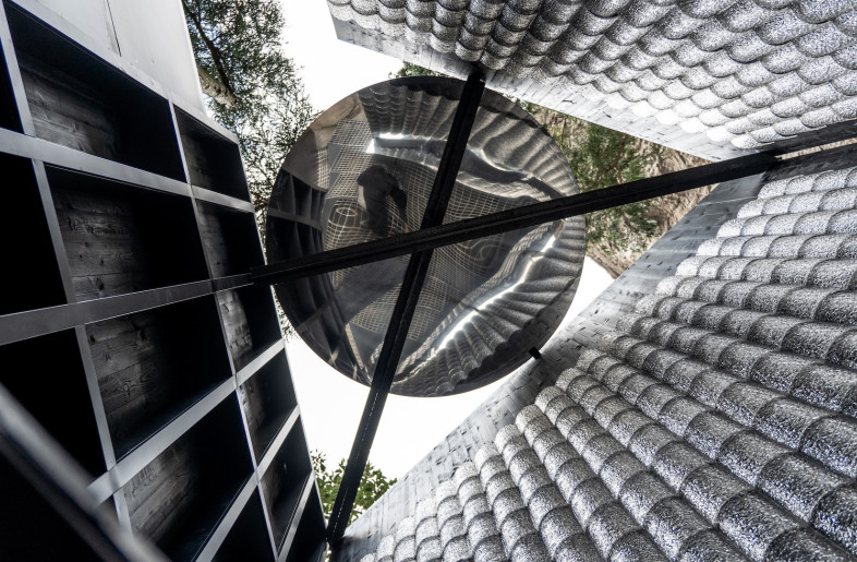 Shaped like a triangular prism, the space is topped with a polished circular object that reflects the visitor's image back down at them while allowing light to enter. - Aptdotapt