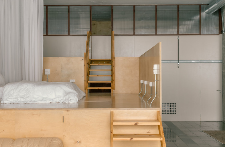 . The volume in the domestic section carves out a sleeping space, with a bed nestled atop an elevated platform and encircled by soft, cream-coloured curtains. - Simone Marcolin