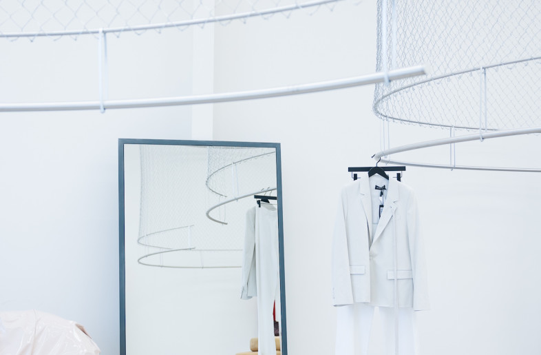 Chain-link fencing is suspended from the ceilings, serving as unexpected garment racks. - Gian Barbarona