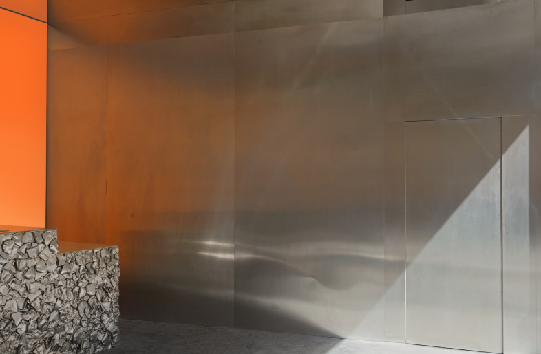Mirrored ceilings amplify the compact interior, reflecting the warm amber wall and metallic surfaces to create an almost infinite visual effect, while poured concrete floors add heft and a grounding element. - Courtesy of Crosby Studios