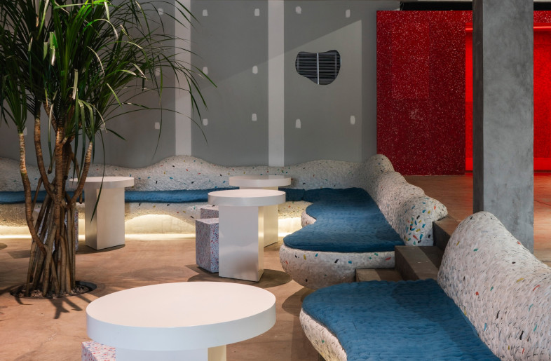 Though largely constructed from steely grey concrete, the space is generously punctuated by bright red shelving and undulating speckled banquettes with cerulean cushions. - Ernest Theofilus