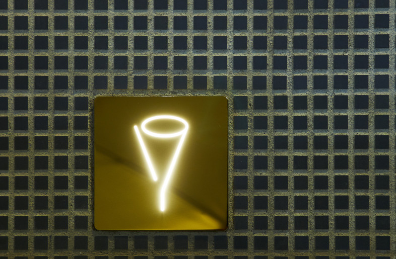 The bar’s name, “19,” is configured into the shape of a cocktail glass and sits above the golden line running across the facade. - Masanori Kaneshita