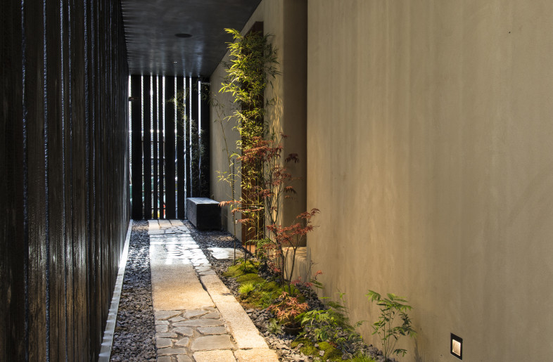 The entrance space is a Japanese-style semi-outdoor alley with a small garden covered with 80% black yakisugi (roasted cypress). - YUHI STUDIO