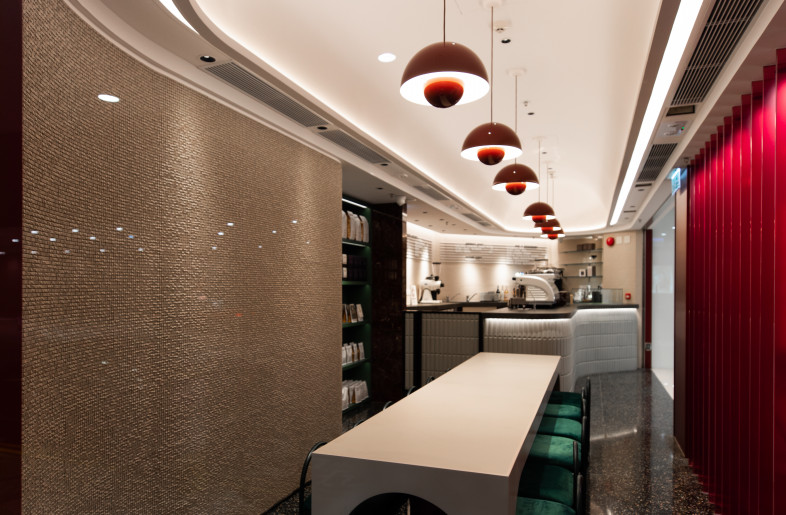 A single edge lit barrel vault illuminates the café tenancy space; it's simple form creates a single point of reference to bring order to the slender and irregularly shaped space. The tenancy is shallow, so a line of red textured glass slats provide a layer of privacy and increases the visibility of the shopfront when viewed at an angle.  A single communal table ensures a clean appearance within the elegant space. - Metagram