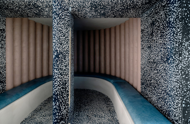 The waiting area is framed in an archway of strong monochromatic terrazzo with molded cement seating arched inset the plaster tube wall with leather seat pad. Full wall of mirror adds a dramatic effect and enhances the feeling of space. - Photo by Ruth Maria Murphy. Design by Kingston Lafferty Design