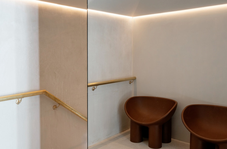Treatment floor waiting area. We designed the first floor as a series of cubes, one set mirrored to maximise light and space and one side a full wall of walnut with inset secret doors into each treatment room. Integrated flos track lighting emits a clean and soft light and leads you through the space - Photo by Ruth Maria Murphy. Design by Kingston Lafferty Design