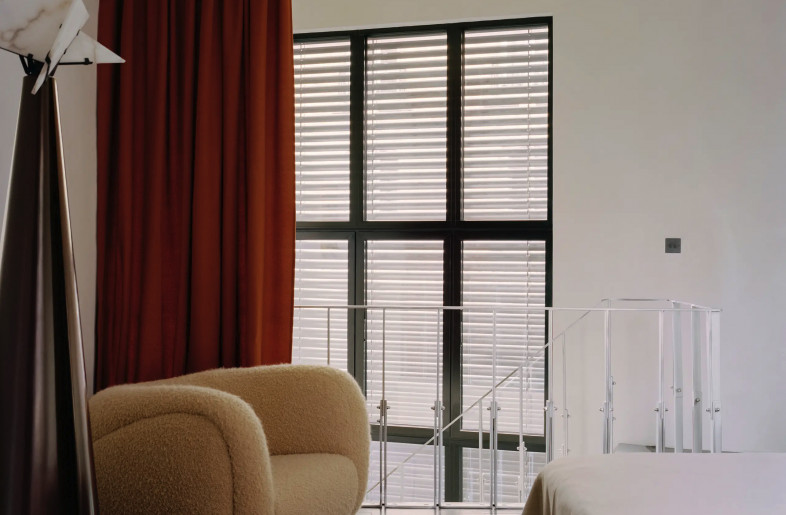 comfortable bedroom with Pierre Chareau floor lamp beside Pierre Augustin Rose armchair and grand atelier style window behind an open stairwell - Christophe Coënon