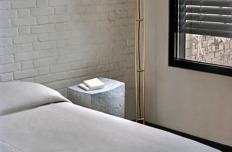 soft light falls on a linen covered bed with a Martin Goerg ceramic bedside table and a designer gold-plated floor lamp by Thomas Duriez - Christophe Coënon