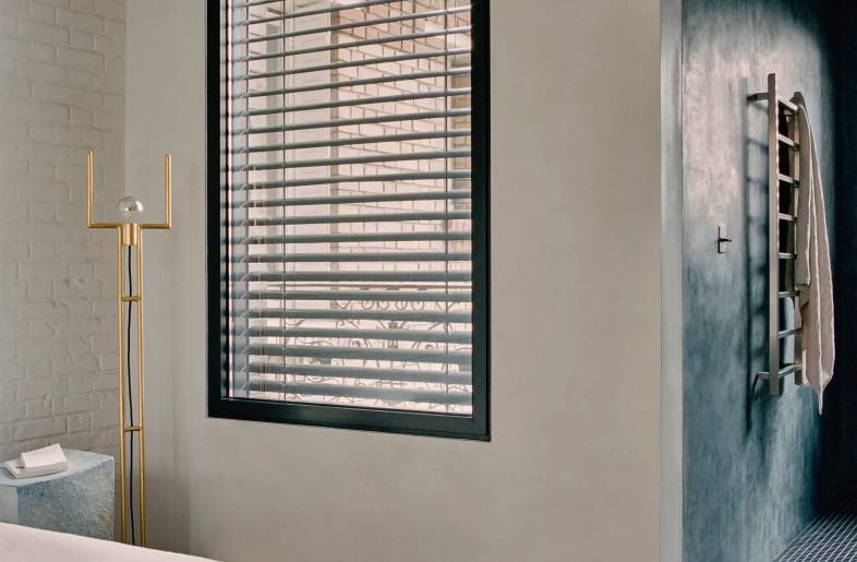 Anthropomorphic collectible floor lamp by Thomas Duriez stands between a linen covered bed and a large contemporary window frame - Christophe Coënon