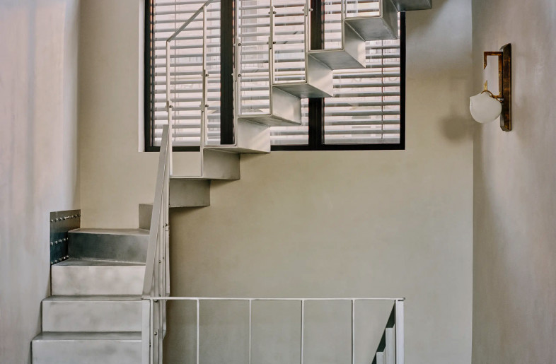Christopher Boots brass wall light hung in an oblique metal stairwell in front of a large, softly lit window - Christophe Coënon