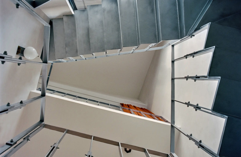 underside view to ceiling of an angular three level staircase void with raw metal stairs and balustrade - Christophe Coënon