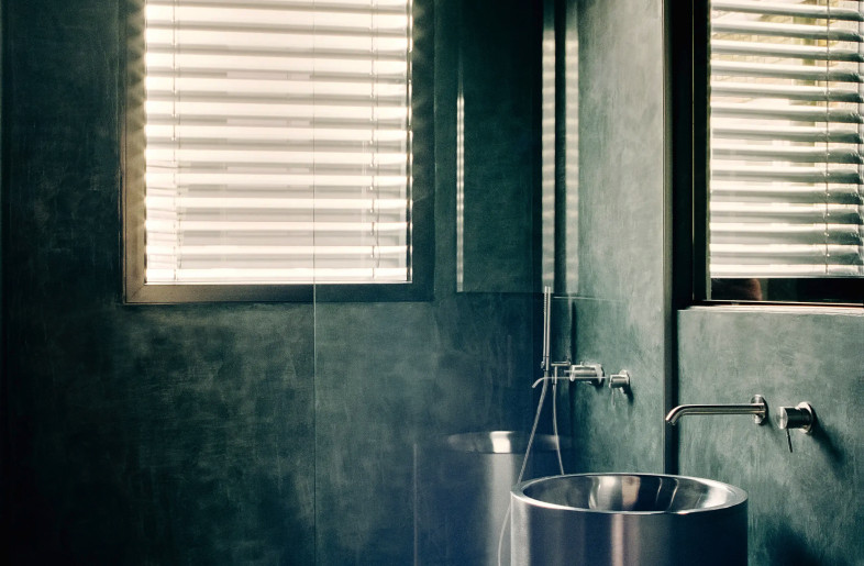 bathroom with dark blue patinated walls and shadowy corners in stark contrast to a stainless steel pedestal sink and neon light - Christophe Coënon