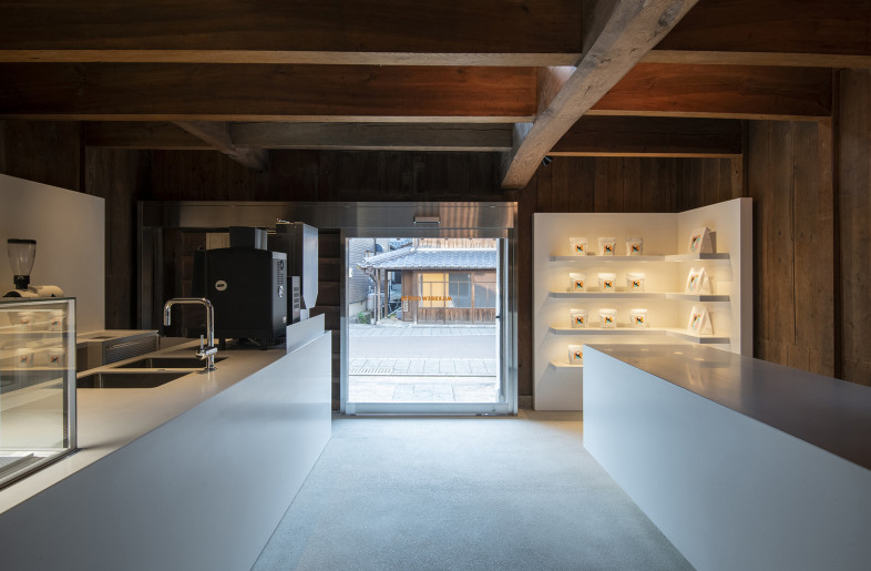 The view from inside toward the street outside. The serving counter is on the left and the display shelf and standing counter on the right. The counter and wall displays were made of white corian inspired by the pure white milk. The existing wooden walls and architectural beams are retained. - Hiroshi Mizusaki