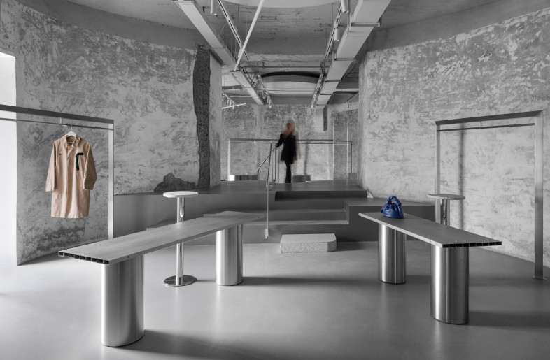 The same dialogue continues throughout the space.  Enter the clothing / Footwear display area on the left, and the space makes the product the main character. The floor type clothes hanger is placed in a more casual and loose way with the exhibition stand. Between the two cylinders on the left, a huge stair crossing stand divides the space and establishes a new connection. - Stairs Showcase